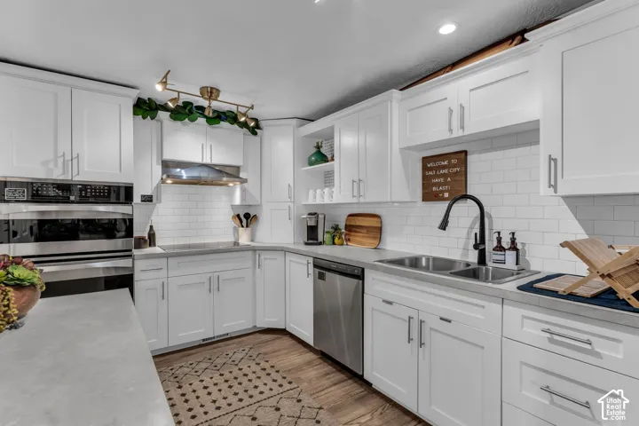 White shaker cabinetry, stainless steel appliances, solid surface countertops, subway tile backsplash, and wood-finish flooring