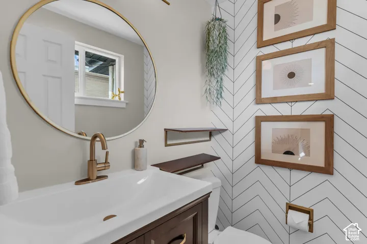 Rectangular undermount sink with a bronze-finish single-handle faucet, round wall-mounted mirror with a gold-finish frame, and white wall tile with a chevron pattern
