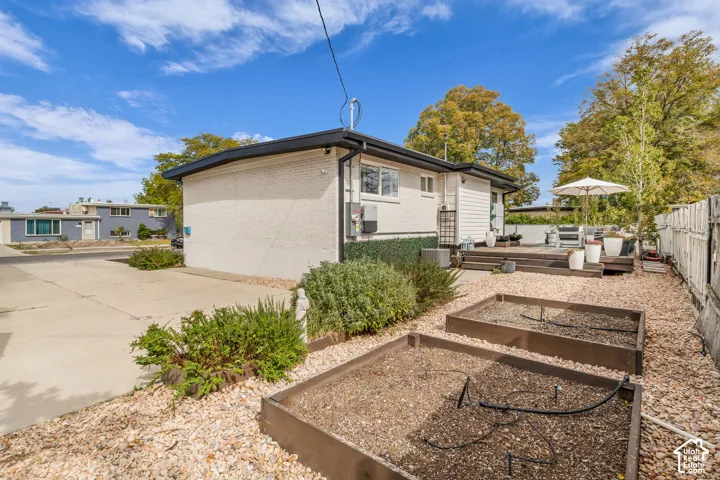 Rear exterior showcasing a multi-level wood deck, white painted brick, and a gravel-covered yard with two raised garden beds