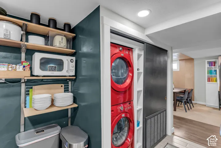 Stacked laundry appliances, built-in shelving, recessed ceiling lighting, and wood-finish flooring