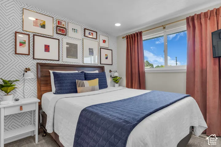 Accent wall featuring geometric pattern, wood-finish headboard, window with white trim, recessed lighting, and wall-mounted light fixture