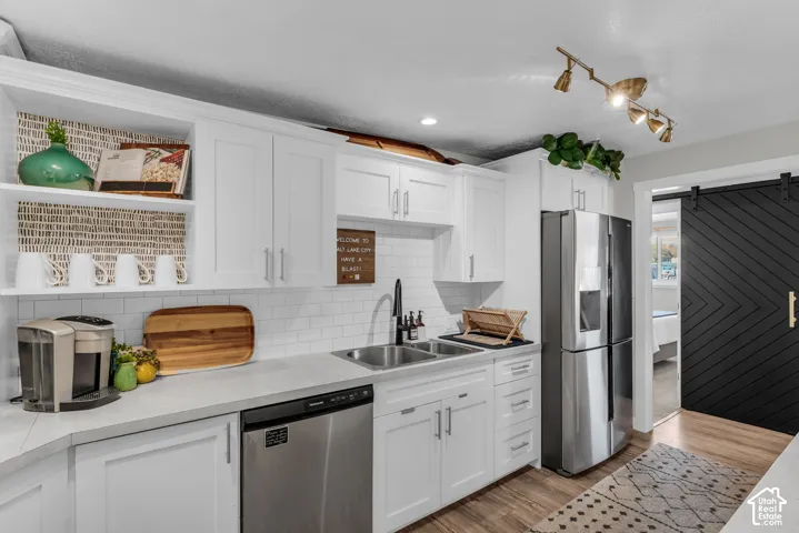 White cabinetry with sleek hardware, dual basin sink, stainless steel appliances, track lighting, and a black sliding barn door