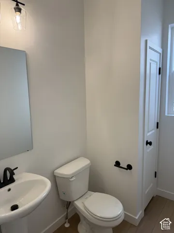 Pedestal sink with a matte black faucet, toilet, and wood-finish flooring