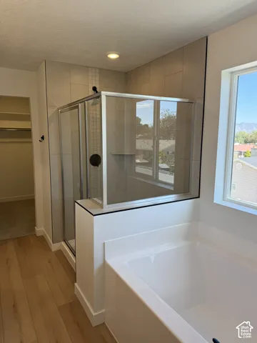 White soaking tub, glass-enclosed shower with tile surround, wood-finish flooring, and recessed lighting