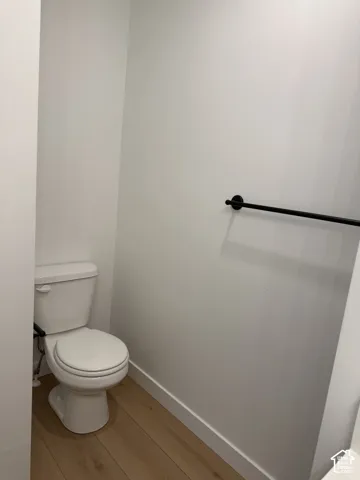 Wood-finish flooring with white baseboards and a white toilet