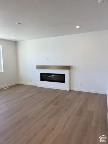 Recessed ceiling lighting, a linear electric fireplace with wood-finish mantel, and wood-finish flooring