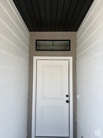 White panel door with matte black hardware, transom window, and horizontal siding