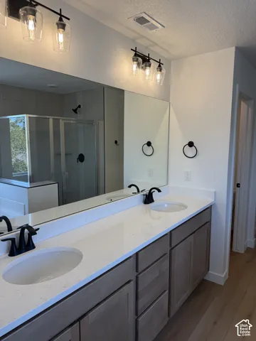 Double vanity with integrated sinks and black matte faucets, under-counter cabinetry, extensive mirror, and wood-finish flooring