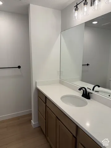 Wood-finish flooring, built-in wooden vanity with ample storage, integrated white sink, solid surface countertop, and modern black faucet