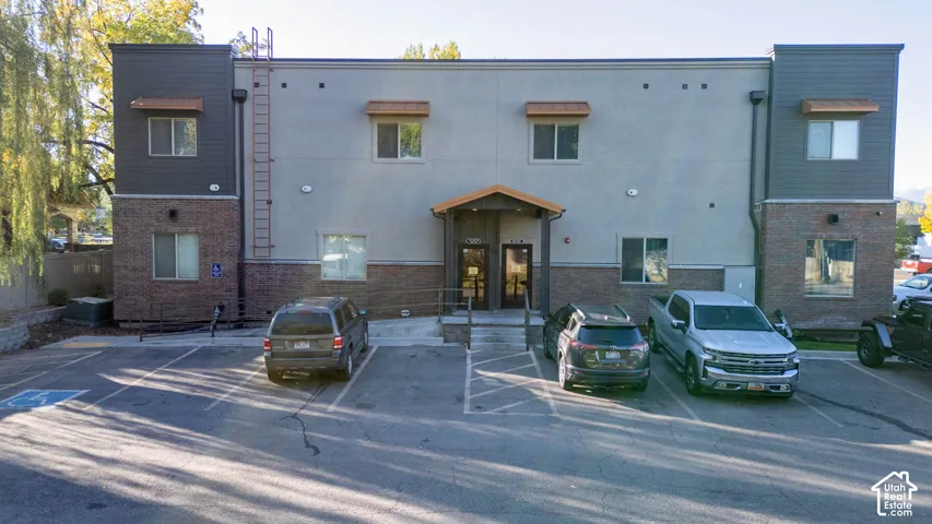 Two-story building featuring brick and panel siding, multiple windows with awnings, and an accessible entrance ramp