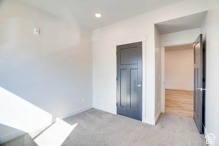 Recessed ceiling lighting, gray carpet flooring, white walls, and dark paneled doors with chrome hardware