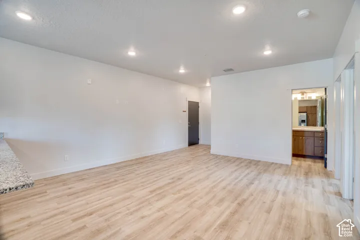 Recessed lighting, wood-finish flooring, white walls, dark gray entry door, and a light-colored speckled countertop