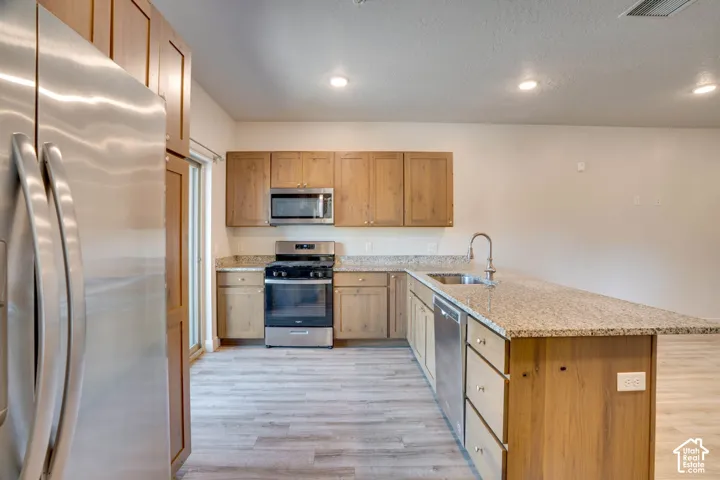 Kitchen featuring wood cabinetry, light-toned granite countertops, stainless steel appliances, and wood-finish flooring