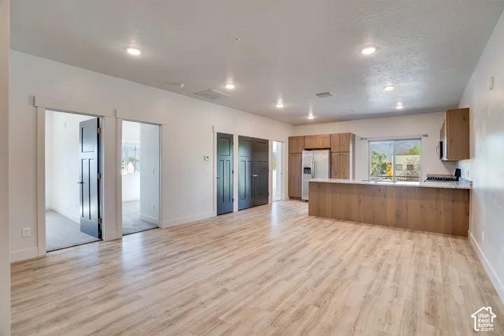 Recessed lighting, wood-finish flooring, kitchen island with seating, stainless steel appliances, and white walls