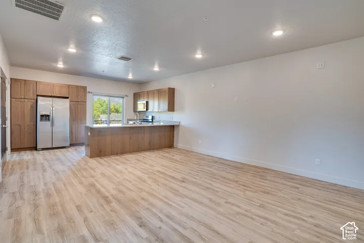 Open-concept living space with wood-finish flooring, recessed lighting, and a kitchen featuring wood cabinetry and stainless steel appliances