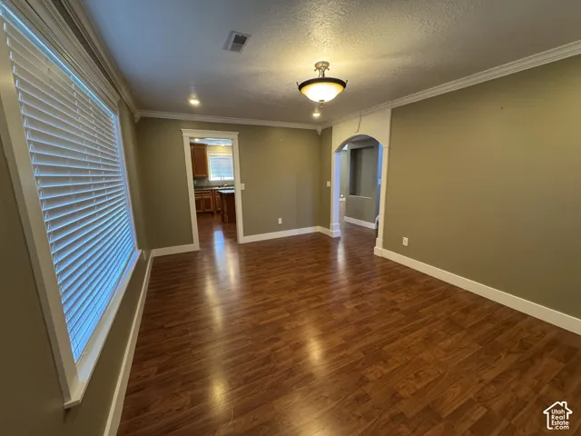 Wood-finish flooring, crown molding, arched doorway, recessed lighting, and a semi-flush mount ceiling fixture