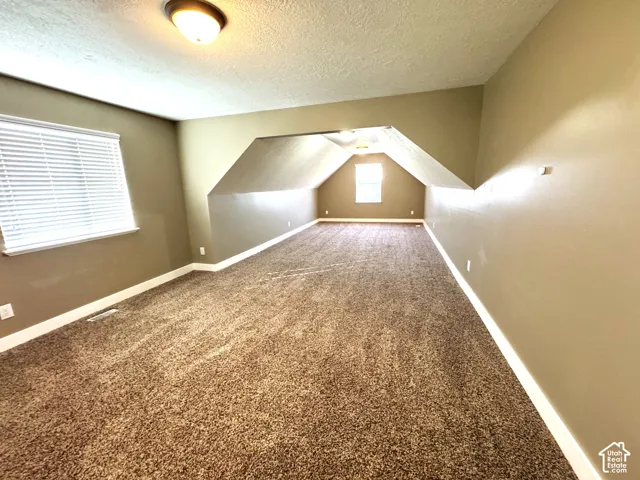 Expansive room featuring textured carpet, multiple windows with blinds, and recessed lighting
