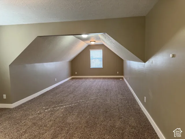 Carpeted room featuring an angled ceiling design, a single window with blinds, and flush-mounted ceiling lighting