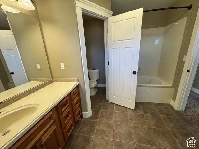 Bathroom featuring a single vanity with wood-finish cabinetry, a large mirror, a separate toilet area, a built-in bathtub with shower, and tile flooring