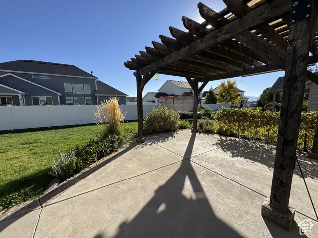 Backyard patio with a wood pergola, stamped concrete, manicured lawn, and perimeter landscaping