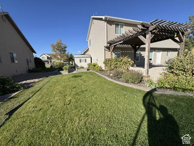 Expansive backyard featuring a manicured lawn, established landscaping, a paved patio, and a wooden pergola structure