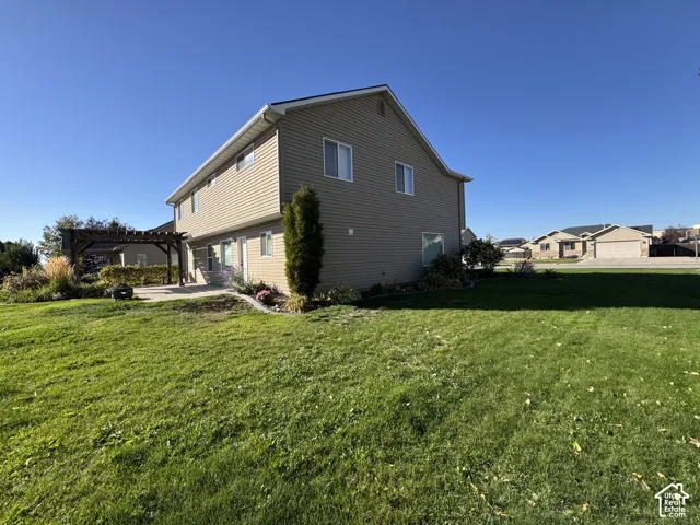 Expansive lawn area with a two-story exterior, mature landscaping, and a patio featuring a wooden pergola