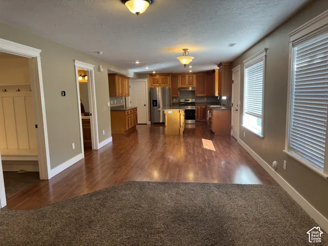 Open-concept living space with wood-finish flooring, a kitchen island, stainless steel appliances, and wood cabinetry