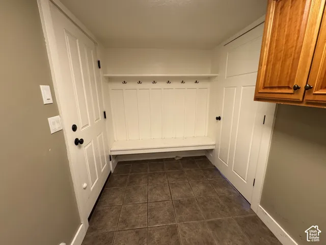 Built-in mudroom bench with coat hooks, white paneled doors, and square tile flooring