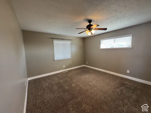 Wall-to-wall carpeting, two windows with blinds, and a ceiling fan with integrated lighting