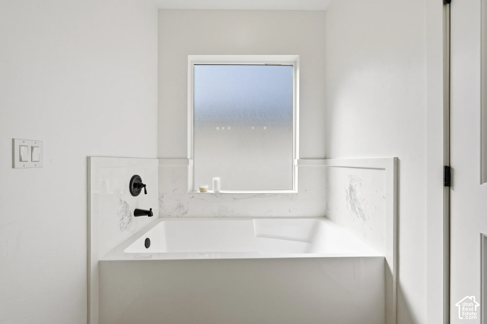 Built-in soaking tub with matte black fixtures, marble-finish surround, and privacy window