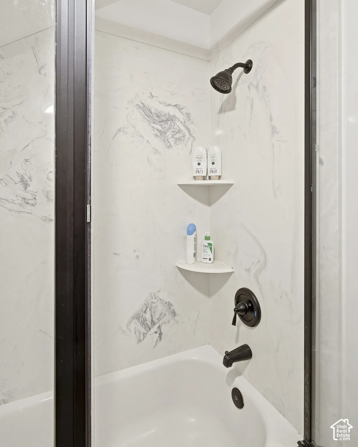 Bathtub and shower combination featuring dark bronze fixtures, a white surround with gray veining, and integrated corner shelving