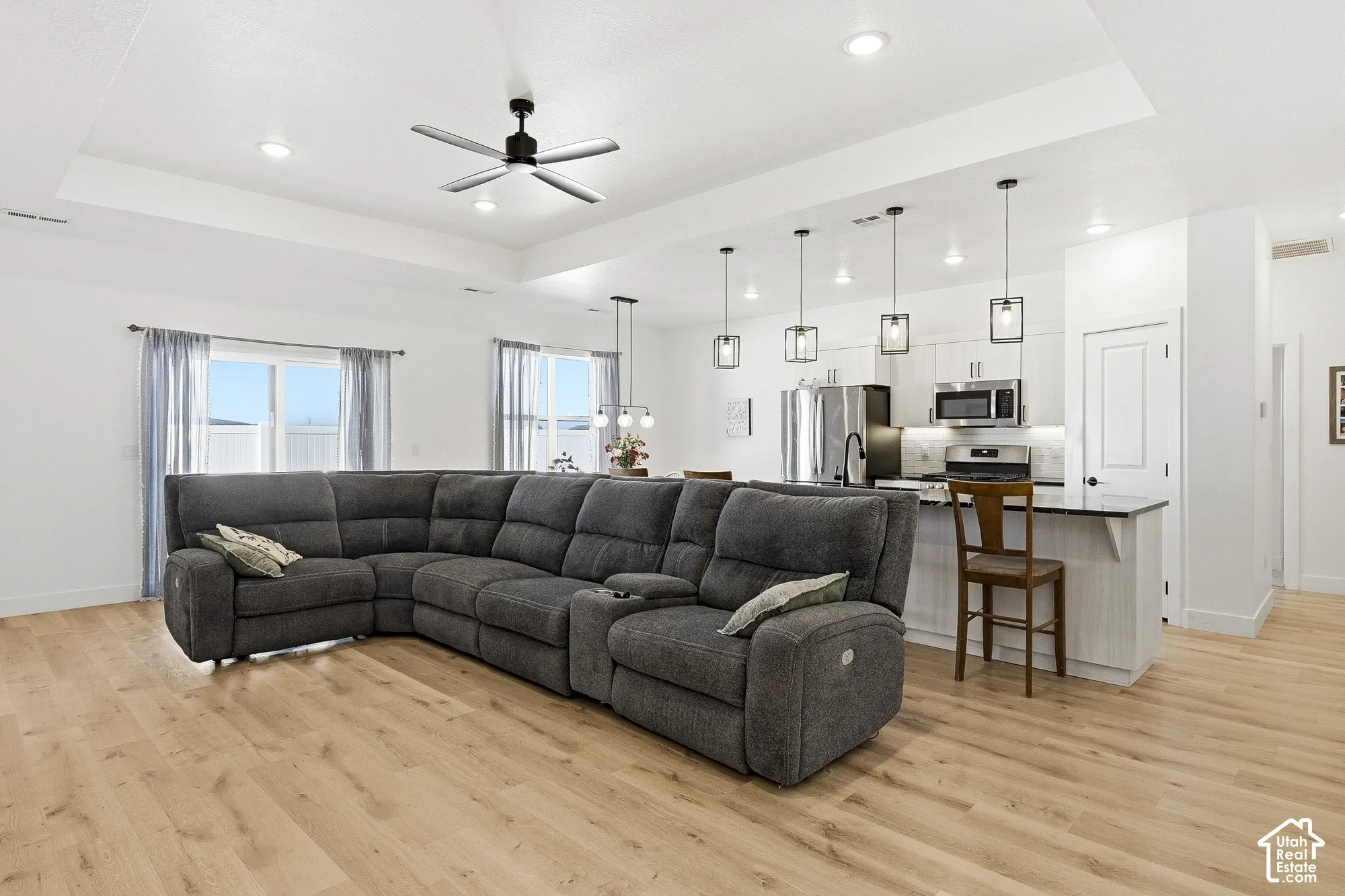 Open-concept living space with wood-finish flooring, recessed lighting, and a tray ceiling
