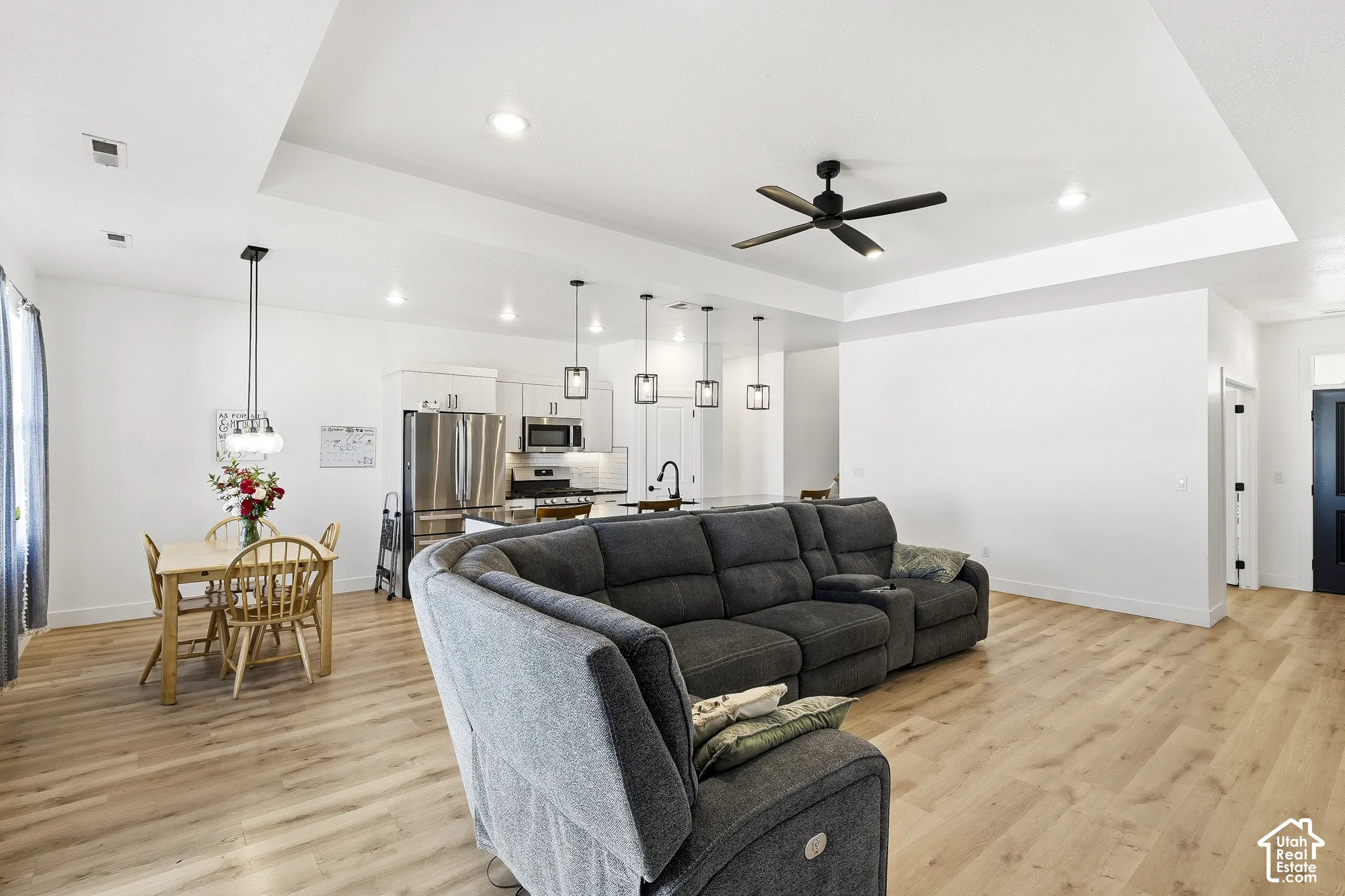Open-concept living area featuring wood-finish flooring, recessed lighting, a tray ceiling, and a modern ceiling fan