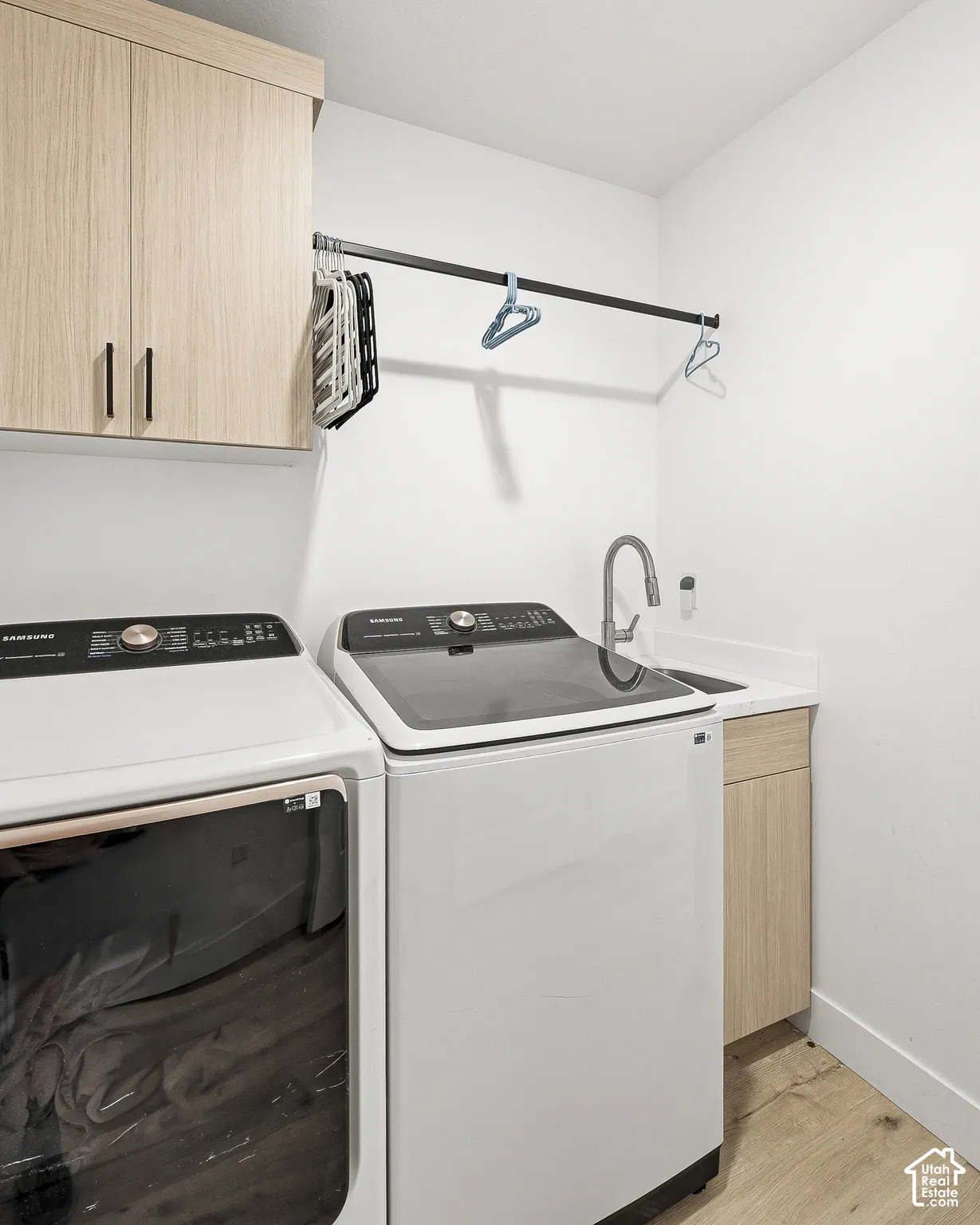 Wood-finish flooring, built-in upper cabinetry, utility sink with a high-arch faucet, and a wall-mounted drying rod