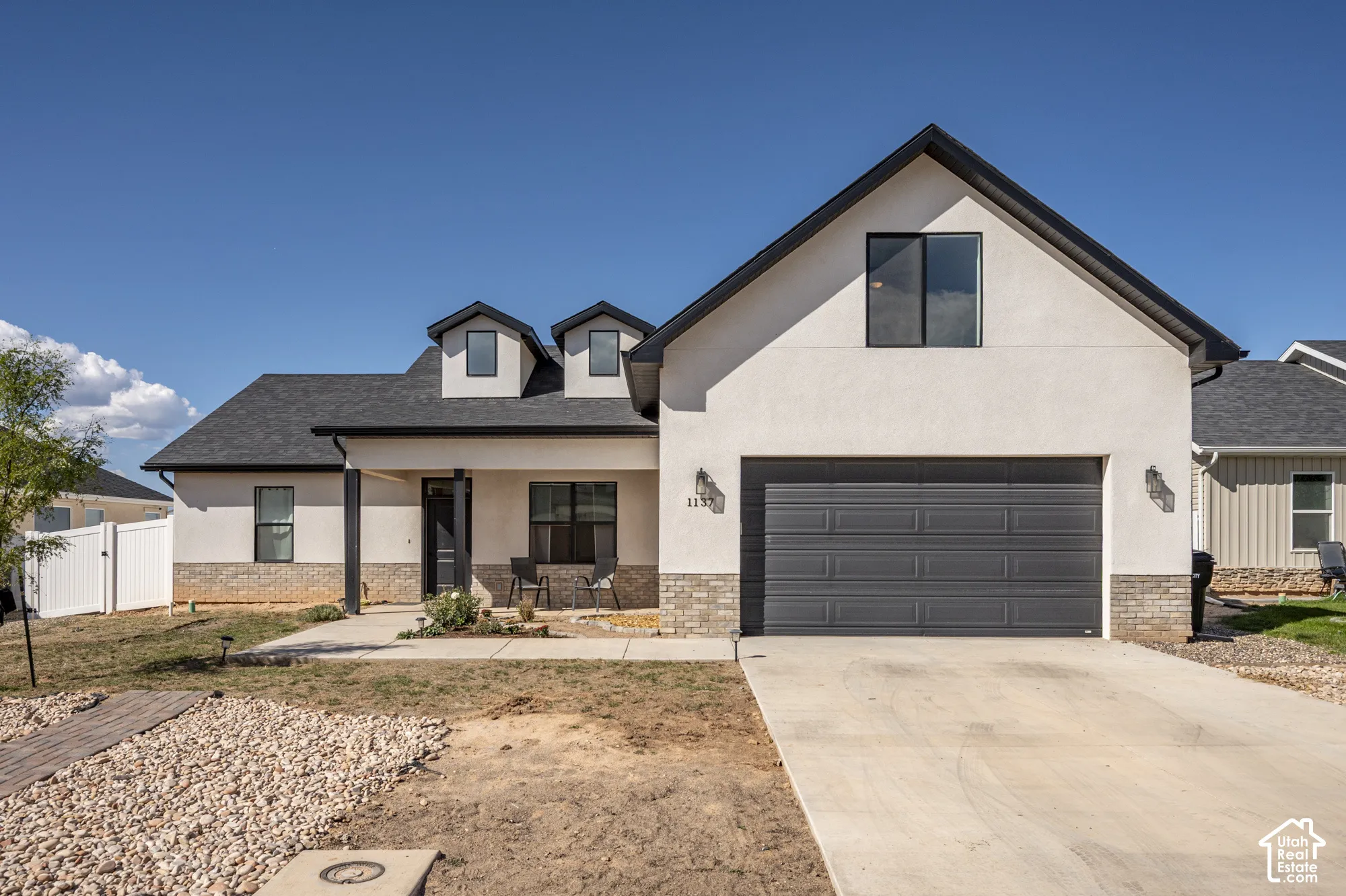Contemporary stucco exterior with brick accents, black-framed windows, and a black shingled roof