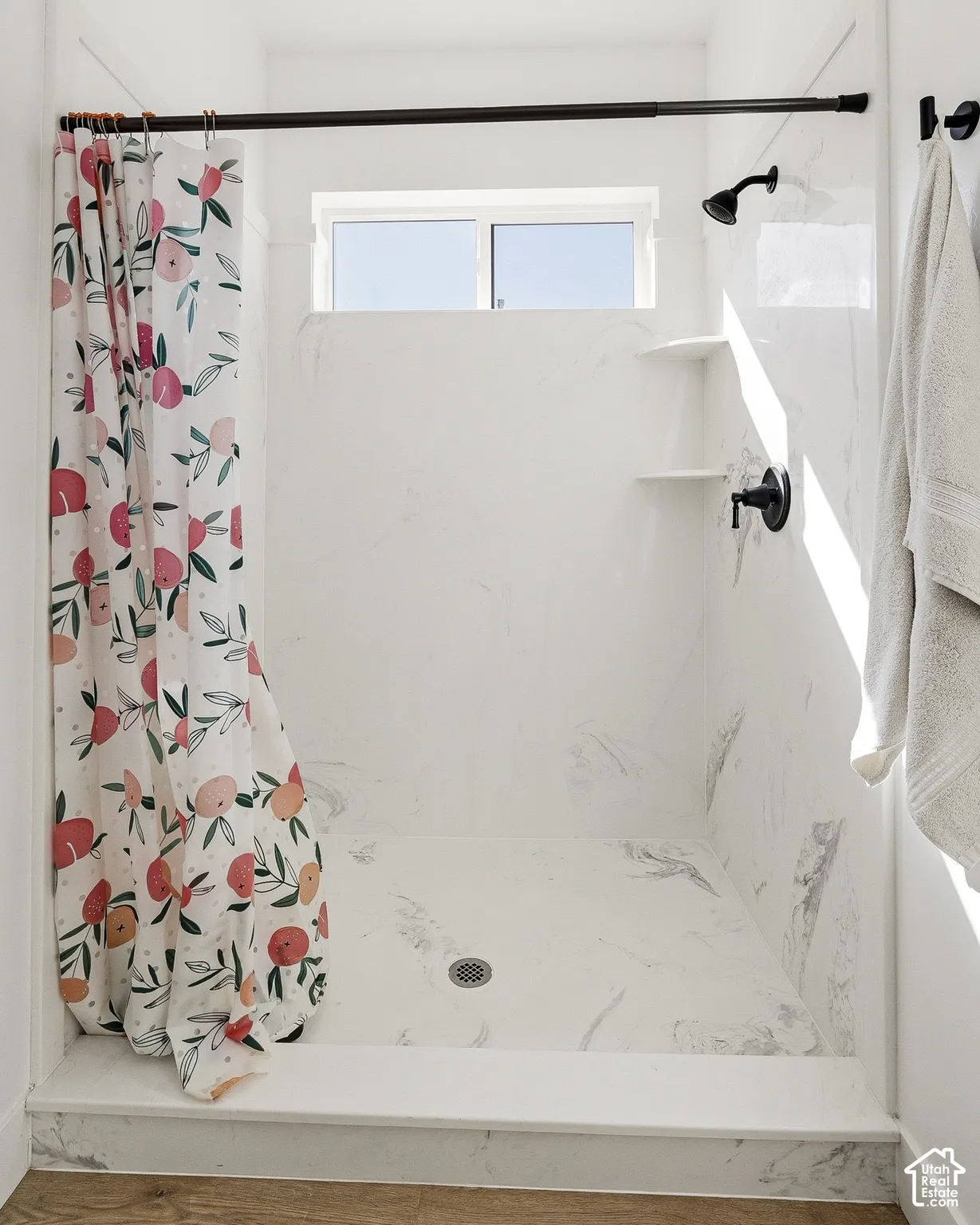 Walk-in shower with white marbled-finish walls, built-in shelving, black fixtures, and an integrated window