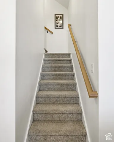 Carpeted staircase featuring a light-toned wood handrail and crisp white walls