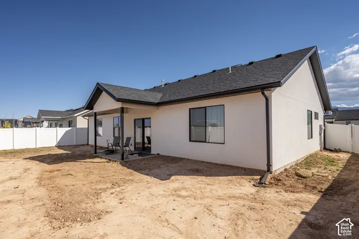Exterior featuring a covered patio, dark asphalt shingle roof, white stucco siding, and black-framed windows