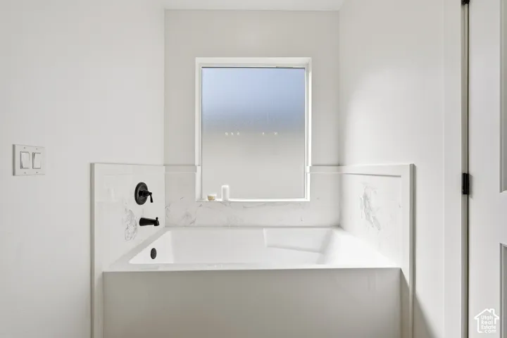 Built-in soaking tub with matte black fixtures, marble-finish surround, and privacy window