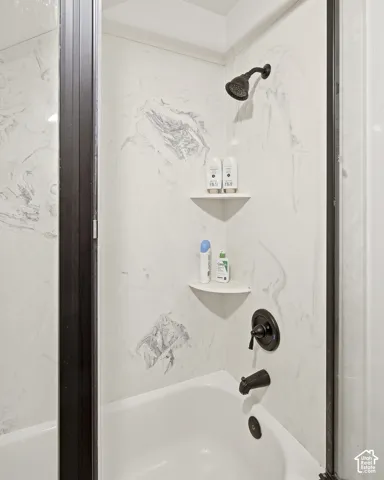 Bathtub and shower combination featuring dark bronze fixtures, a white surround with gray veining, and integrated corner shelving