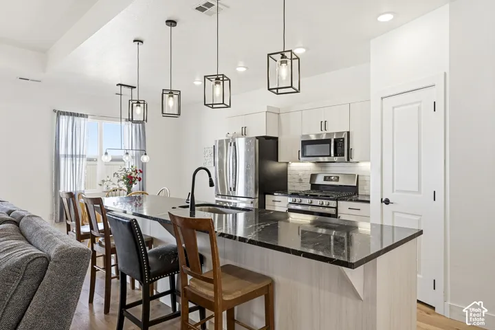 Kitchen featuring an expansive island with a dark countertop, white shaker cabinetry, stainless steel appliances, and pendant lighting