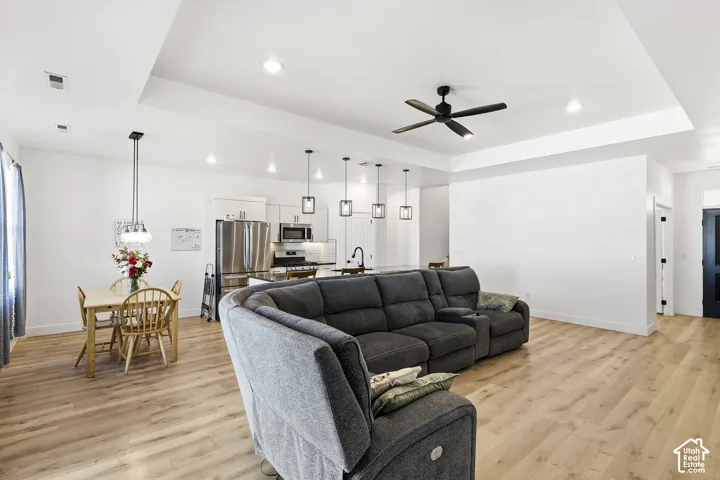 Open-concept living area featuring wood-finish flooring, recessed lighting, a tray ceiling, and a modern ceiling fan