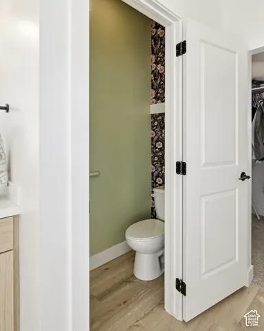 Light wood-finish flooring, white paneled door with matte black hardware, and toilet with a partial floral accent wall
