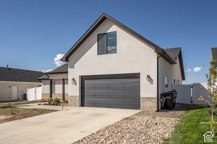 Contemporary stucco exterior with a dark-paneled garage door, complementary stone veneer accents, and a contrasting dark shingle roof