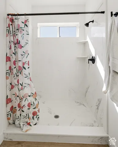 Walk-in shower with white marbled-finish walls, built-in shelving, black fixtures, and an integrated window