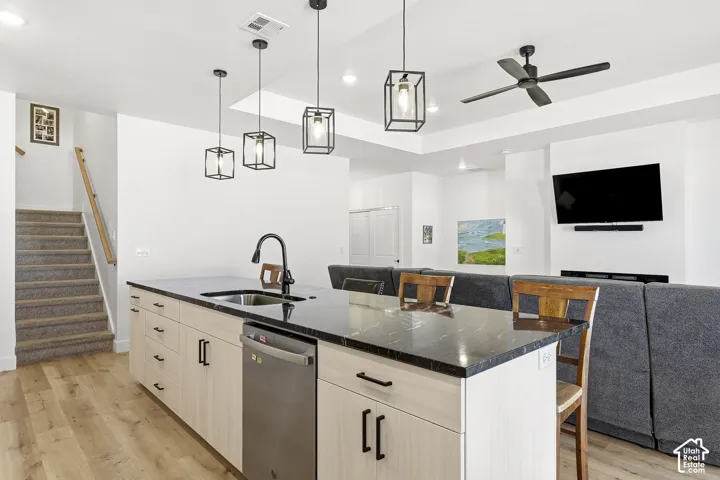 Kitchen island featuring a stainless steel sink with a matte black faucet, integrated dishwasher, light wood-finish cabinetry, and a dark stone countertop