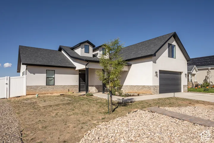 Modern exterior featuring white stucco and stone veneer accents, dark shingled roof, black-framed windows, and an integrated garage with a dark door