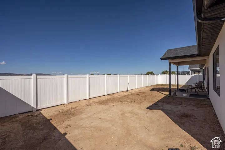 Expansive backyard featuring a white privacy fence, covered patio with dark columns, and dark-framed windows