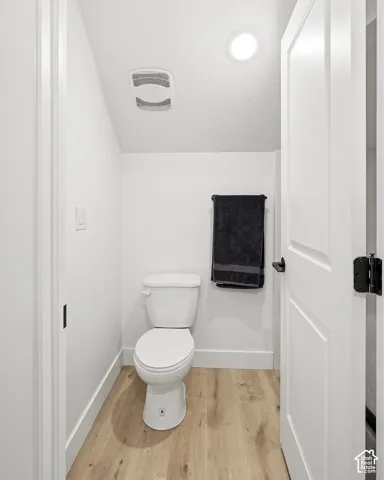 Recessed lighting, wood-finish flooring, white paneled door with black hardware, white toilet, and white walls