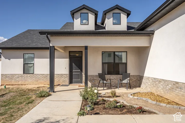 Stucco and brick exterior with black framed windows, a covered entry, and dormer windows